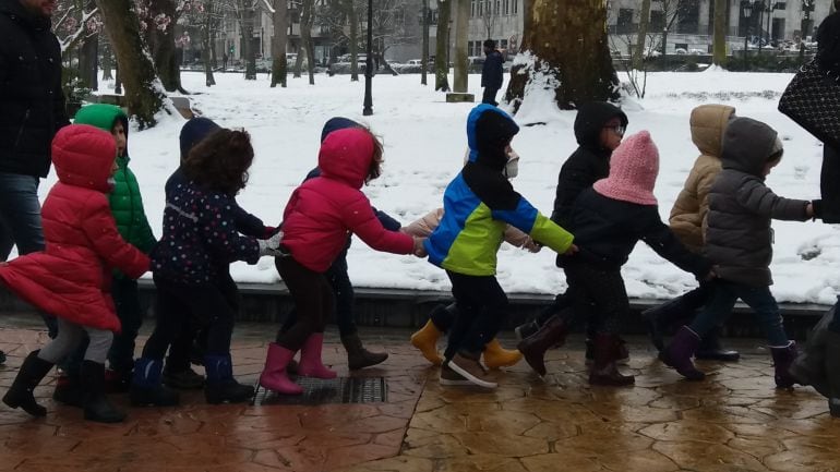 Un grupo de escolares, bien abrigados, atreviesa el Campo de San Francisco con los parterres cubiertos de nieve.