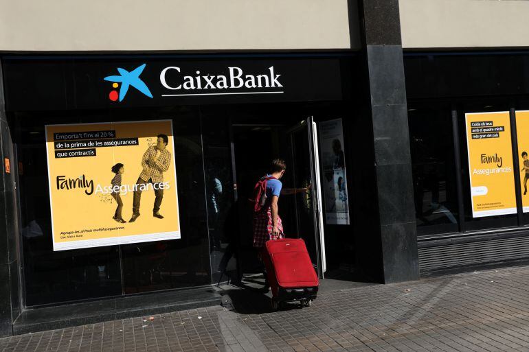 A hombre entra con una maleta en una oficina de Caixabank en Barcelona