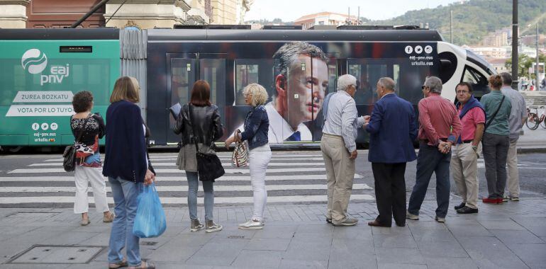 Ciudadanos observan el tranvía de Bilbao con publicidad electoral del PNV. 