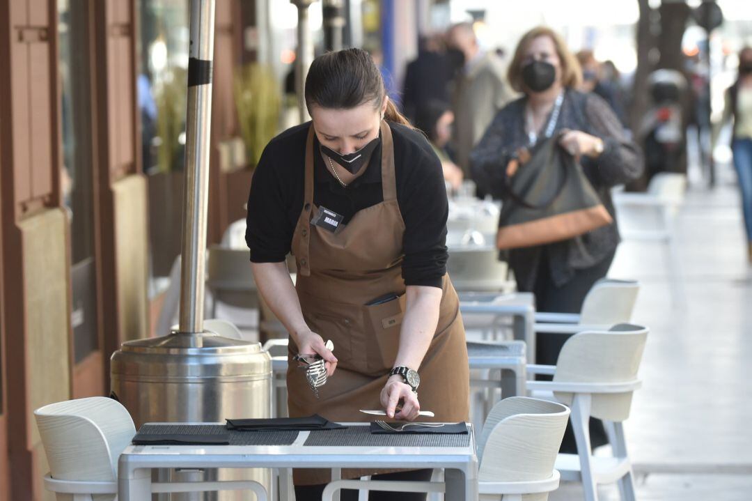 Una camarera preparando las mesas de una terraza