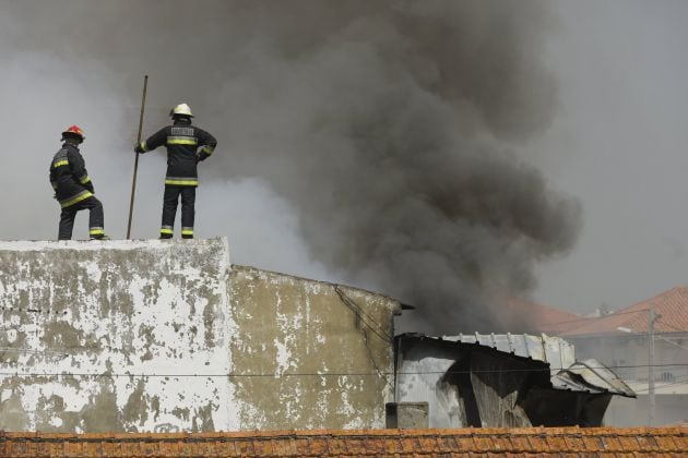 Bomberos trabajan en las labores de extinción de varios edificios en llamas tras estrellarse una avioneta junto a un supermercado en Tires.