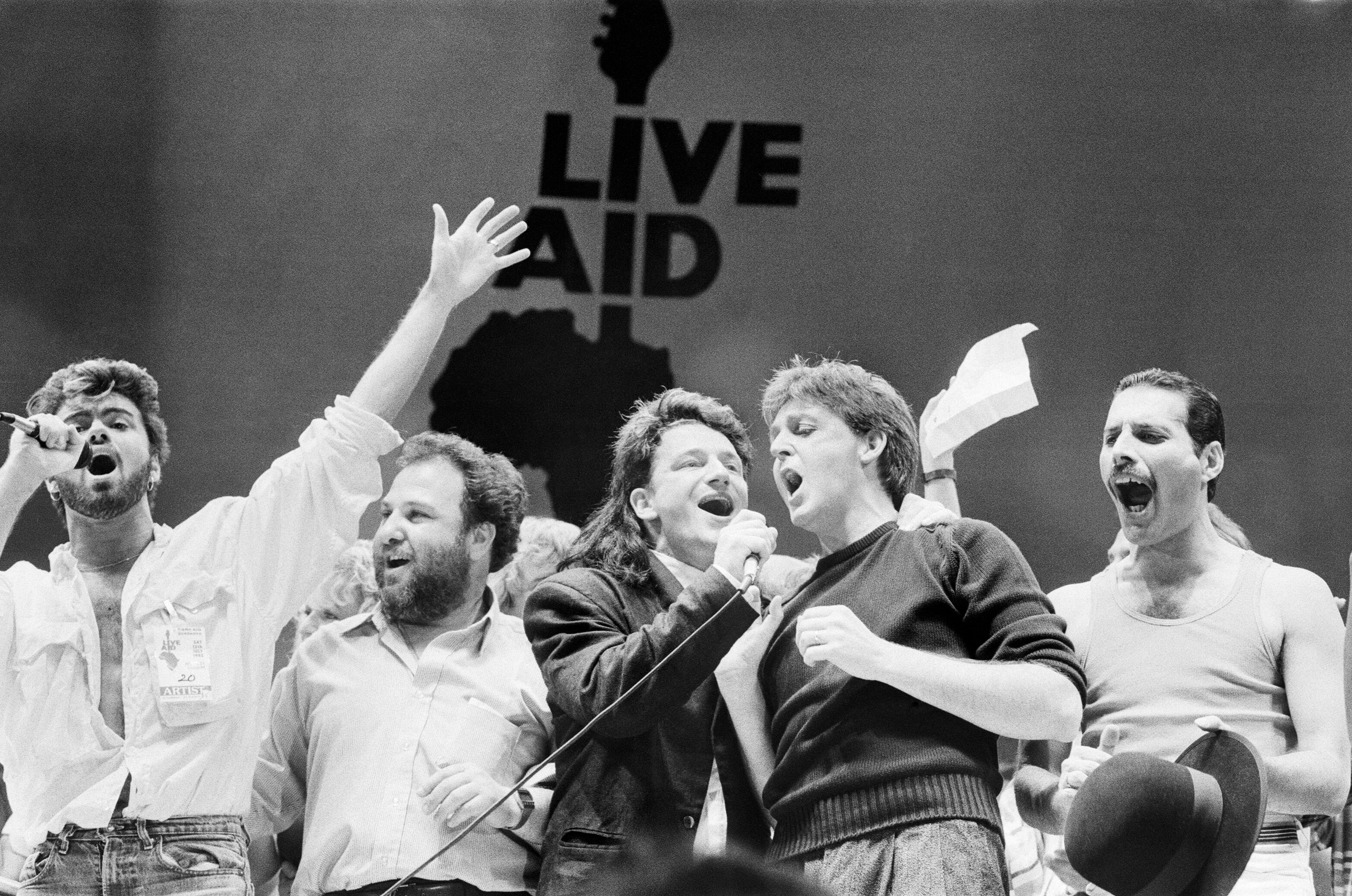 La imagen muestra a George Michael, el promotor Harvey Goldsmith, el cantante de U2, Bono, Paul McCartney y Freddie Mercury, actuando en el escenario durante la final del concierto en Wembley. Daily Mirror/Mirrorpix/Getty Images.