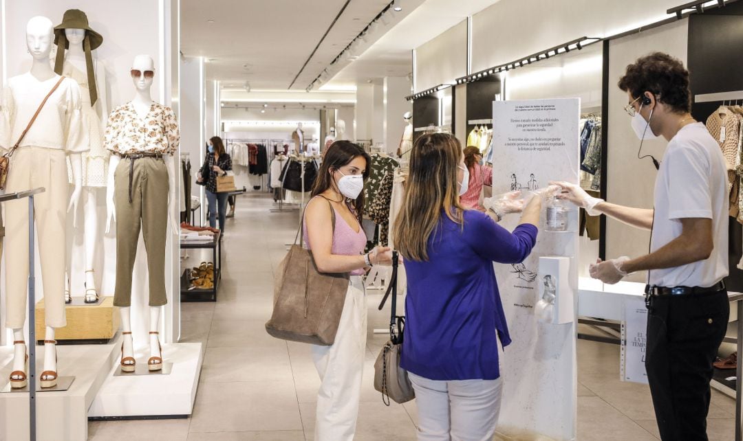 Dos clientas se desinfectan las manos con gel hidroalcohólico a la entrada de una tienda de ropa.