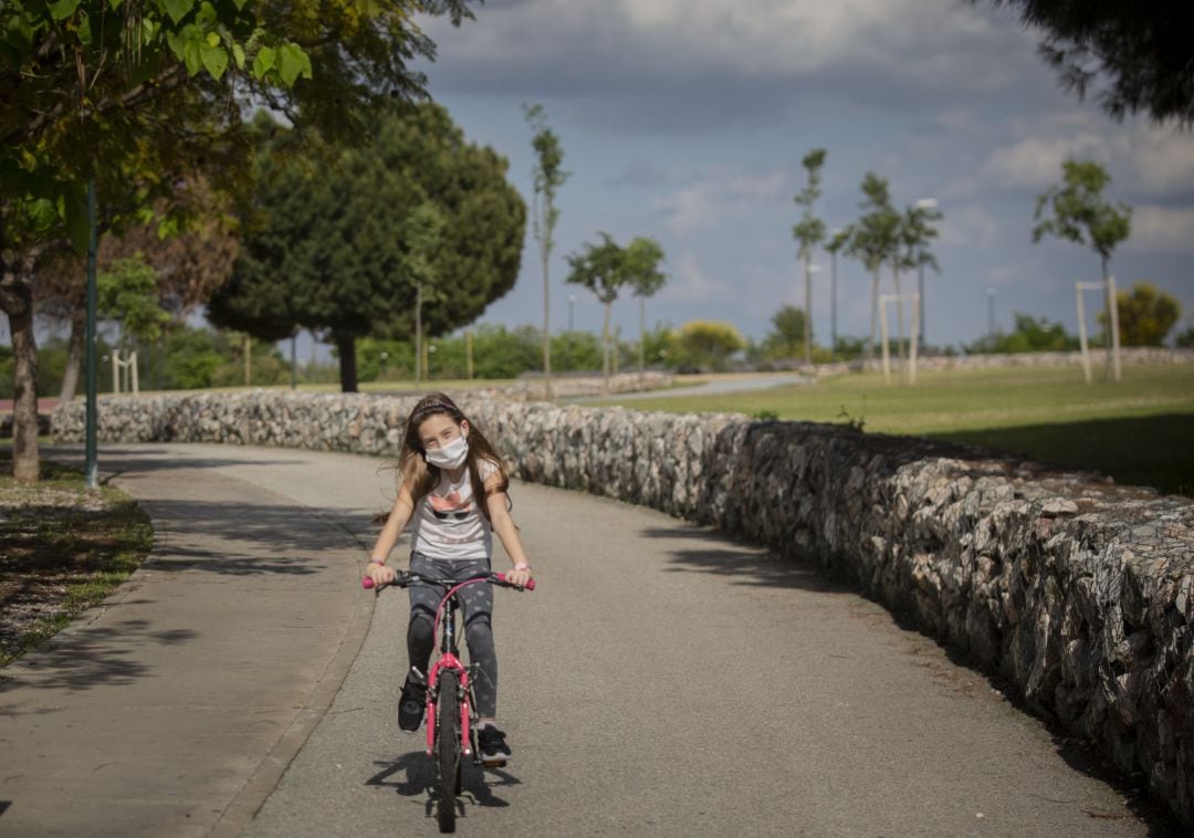 Una niña con mascarilla monta en bicicleta por el parque en el tercer día de desconfinamiento de niños.