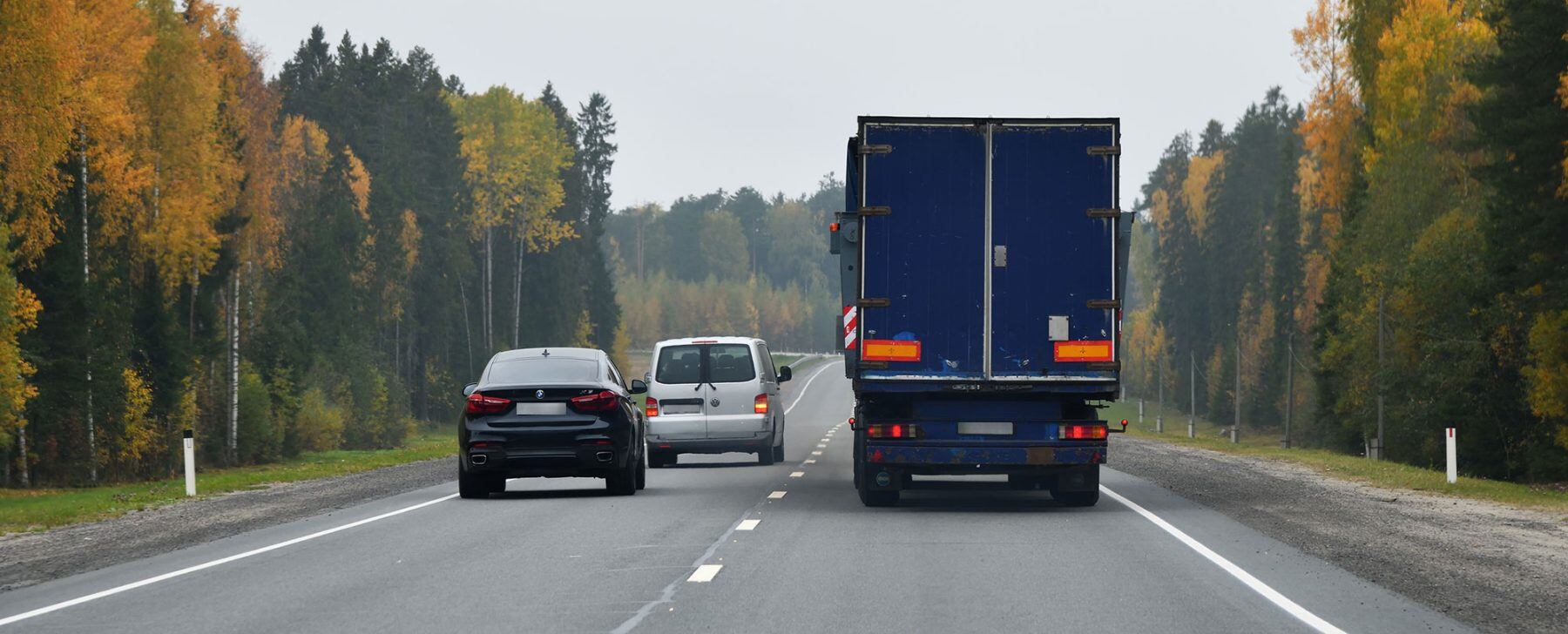 Dos coches adelantan a un camión en una carretera convencional.