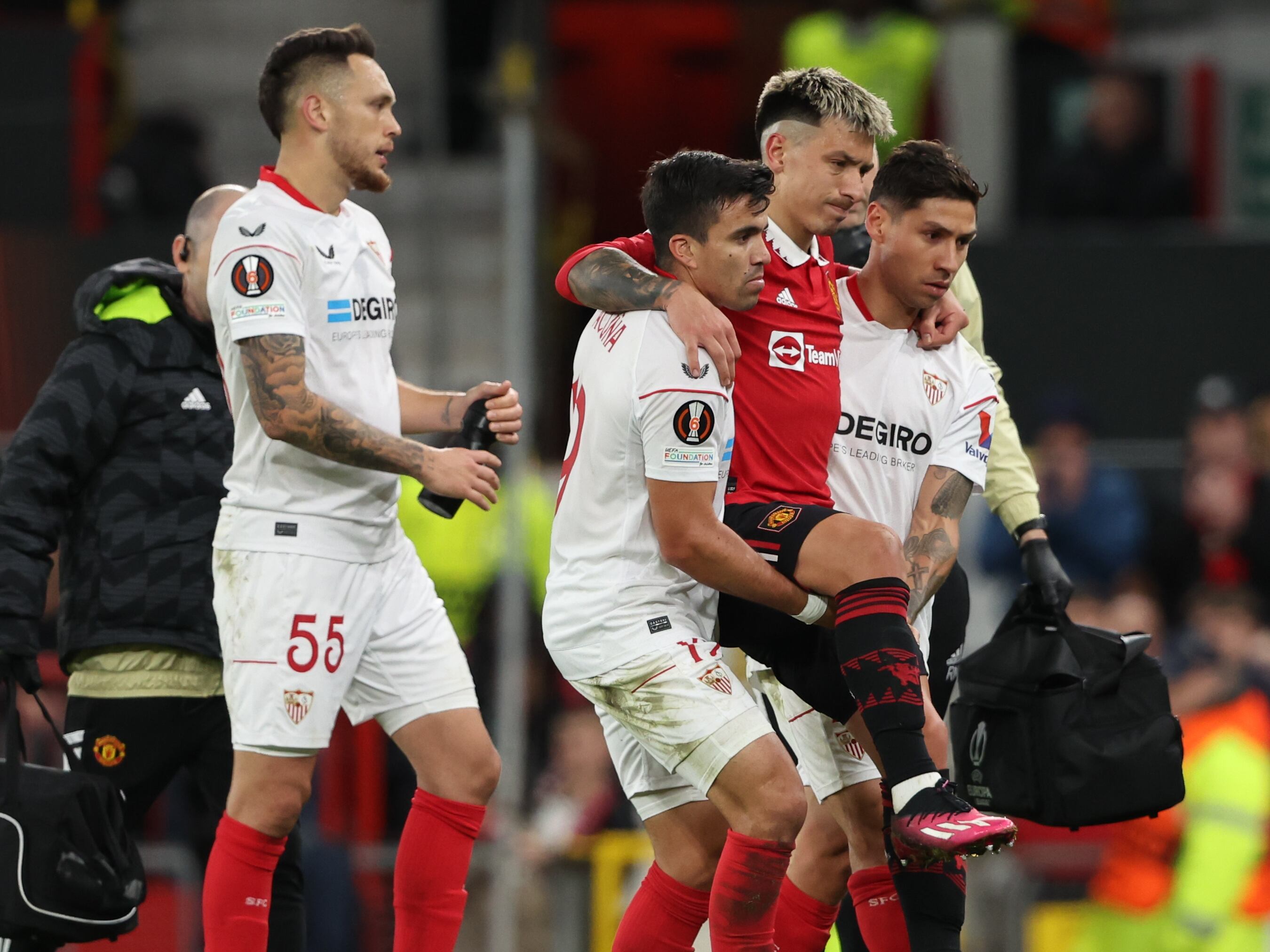 Marcos Acuña y Gabriel Montiel, del Sevilla, ayudan a Lisandro Martínez a salir de campo tras su lesión