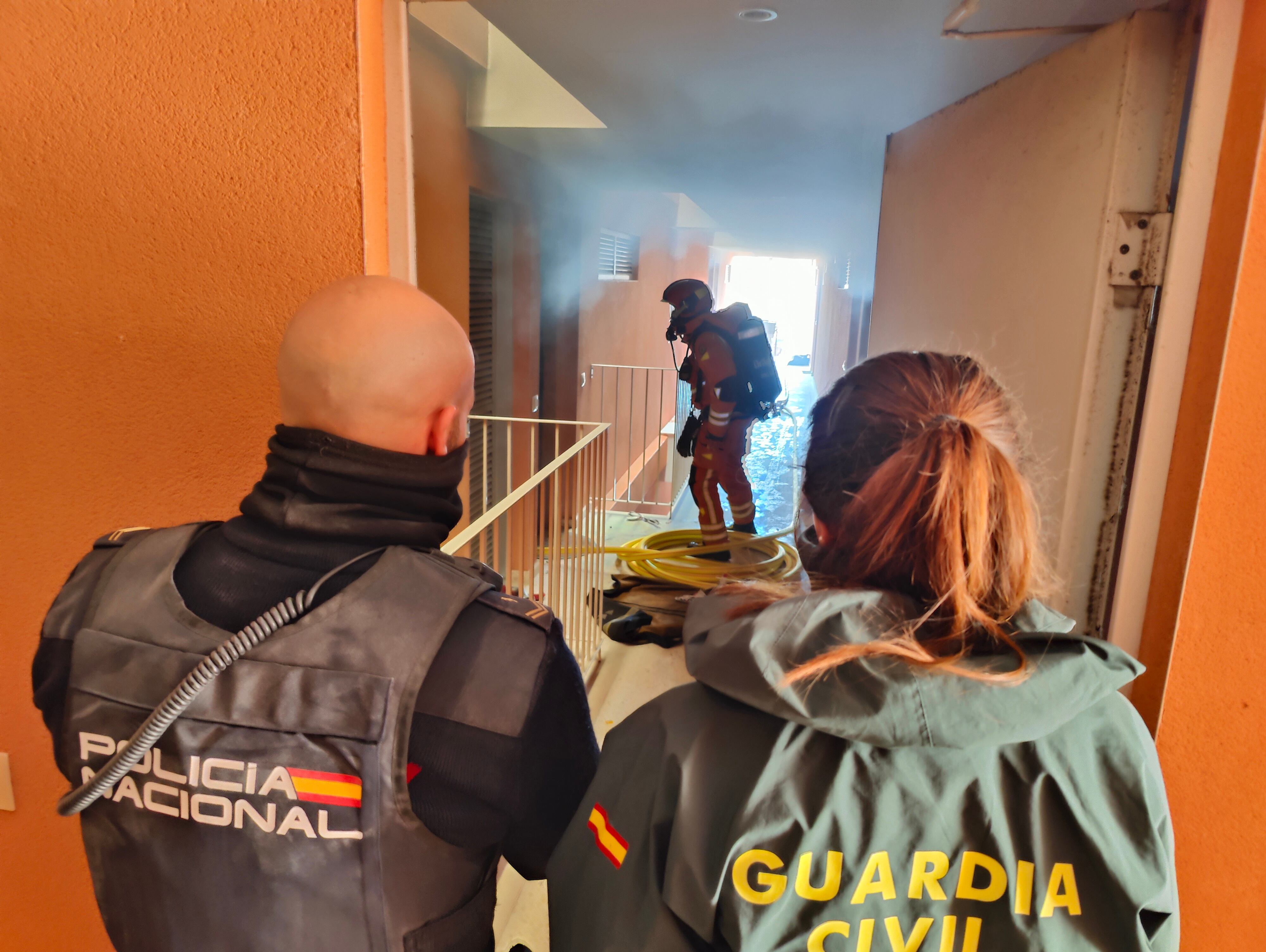 Un bombero actúa en la vivienda incendiada en Gandia ante la mirada de agentes de la Policía Nacional y la Guardia Civil.