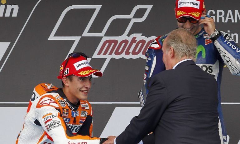 El piloto español Jorge Lorenzo (detrás), en el podio tras recibir el trofeo de manos del rey Juan Carlos, que saluda a su compatriota Marc Márquez (i), segundo clasificado, tras proclamarse vencedor del Gran Premio de España de MotoGP