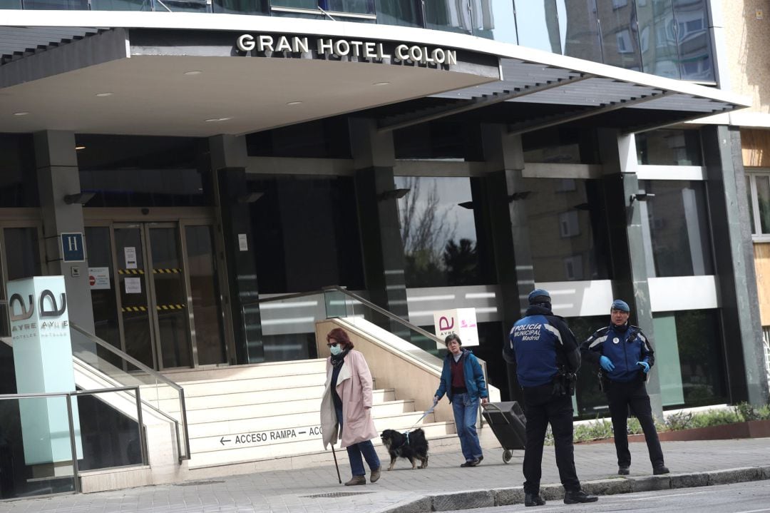 Dos personas pasan por delante del Hotel Colón, en cuya puerta pueden verse dos policías.