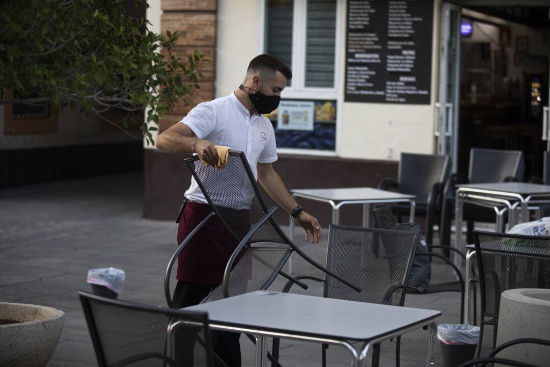 Un camarero recoge el mobiliario de la terraza de un bar