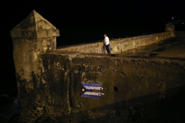 A Cuban flag is seen painted as a man looks at the ocean from the Malecon, following the announcement of the death of Cuban revolutionary leader Fidel Castro, in Havana, Cuba November 27, 2016. 