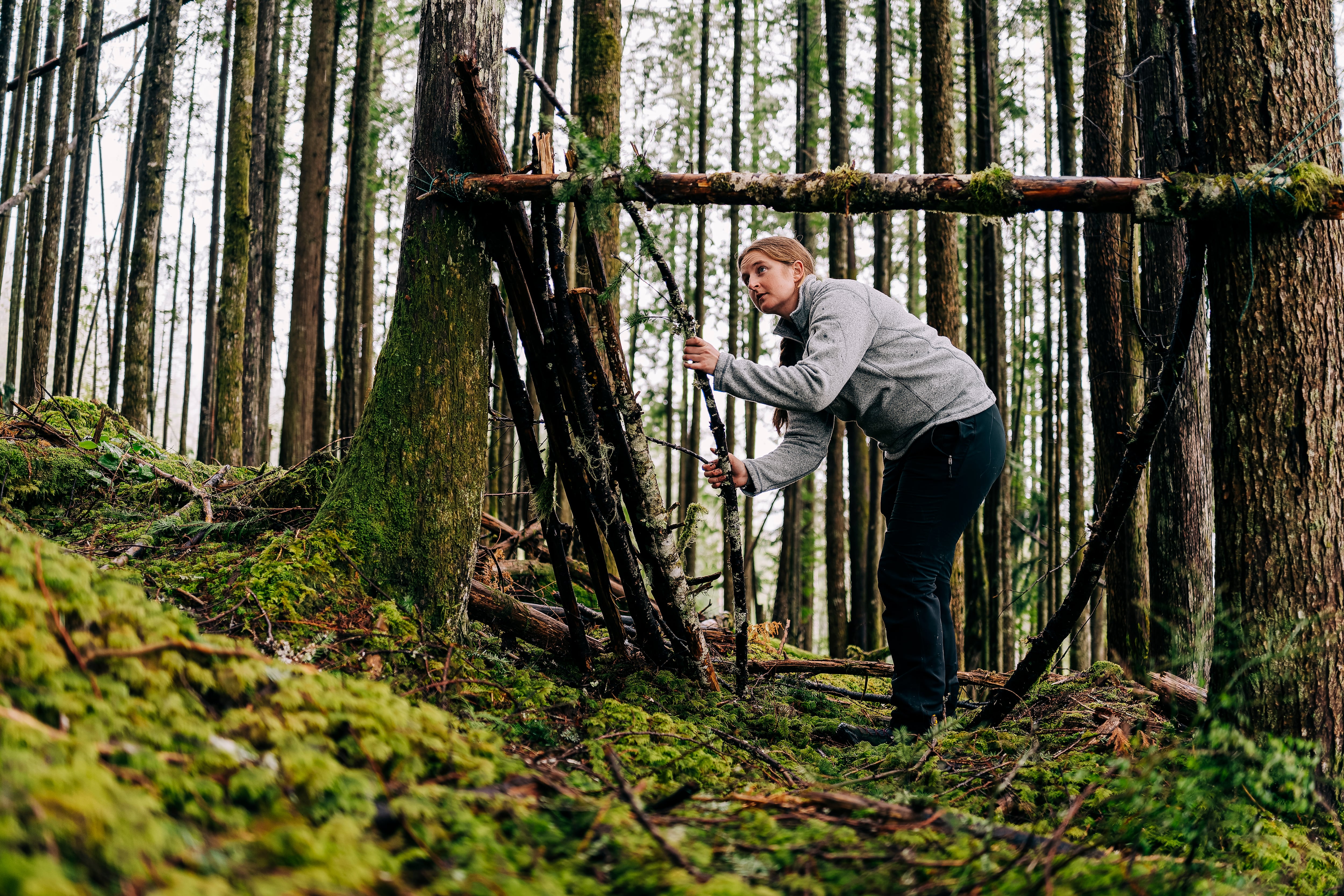 Una joven construyendo un refugio en un bosque.