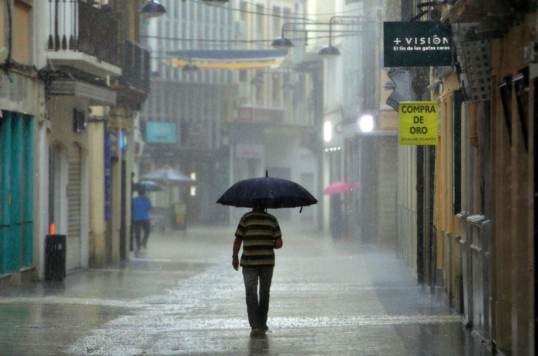 Un hombre camina bajo una intensa lluvia por el centro de la ciudad de Gandía.