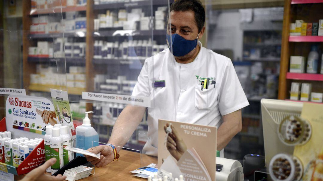 Un farmacéutico entrega una mascarilla a un cliente.