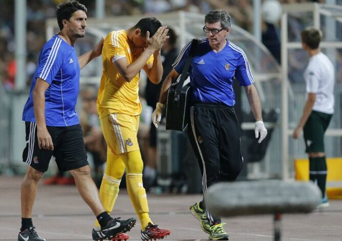 Rulli se retira lesionado del campo lamentándose mientras es consolado por Roberto Navajas, entrenador de porteros de la Real, y el médico realista, González de Suso.