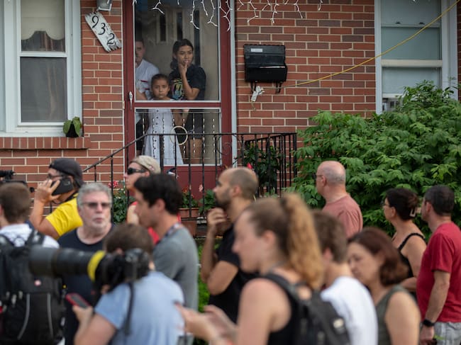 Una familia mira afuera de la puerta de su casa cerca del domicilio de la madre del hombre detenido.