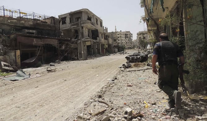 Un soldado del ejército sirio lleva su arma mientras camina por una calle rodeada de edificios dañados en Arbaeen