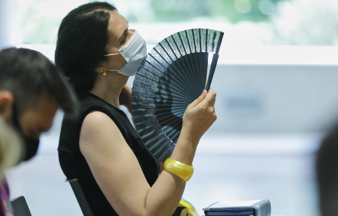 Una mujer con mascarilla se abanica