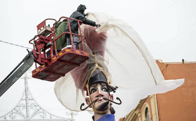 Un trabajador del taller del artista fallero Vicente Llácer protege con plastico la cabeza de una de las figuras centrales de la falla Cuba