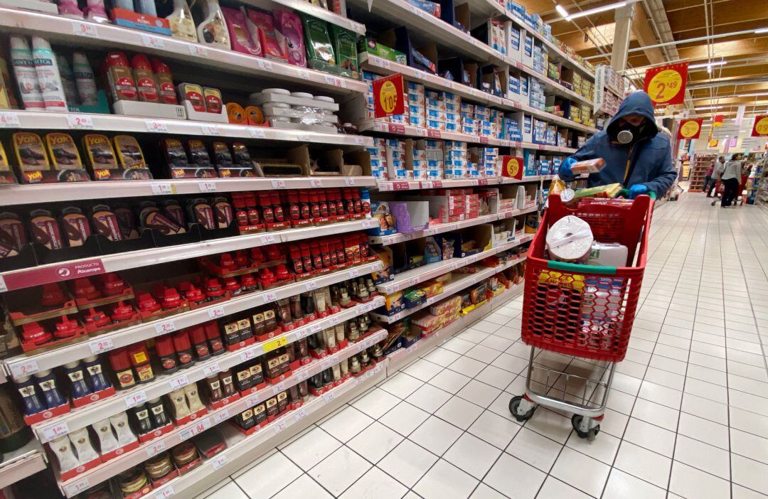 Un hombre cubierto con una mascarilla coge productos de las estanterías de un supermercado de Madrid.