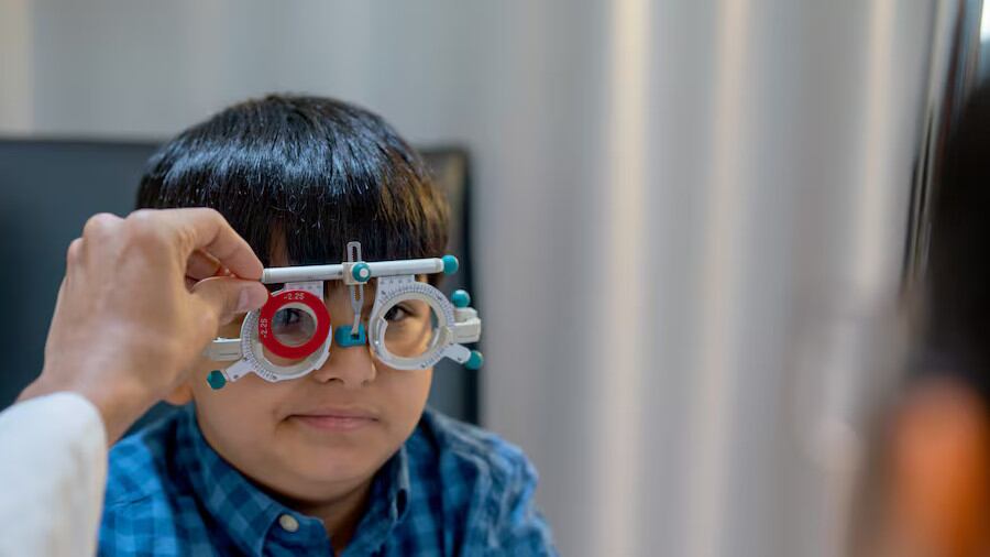 Las manos del personal óptico tocan y sostienen las herramientas oculares que usa un niño pequeño para revisar los ojos.