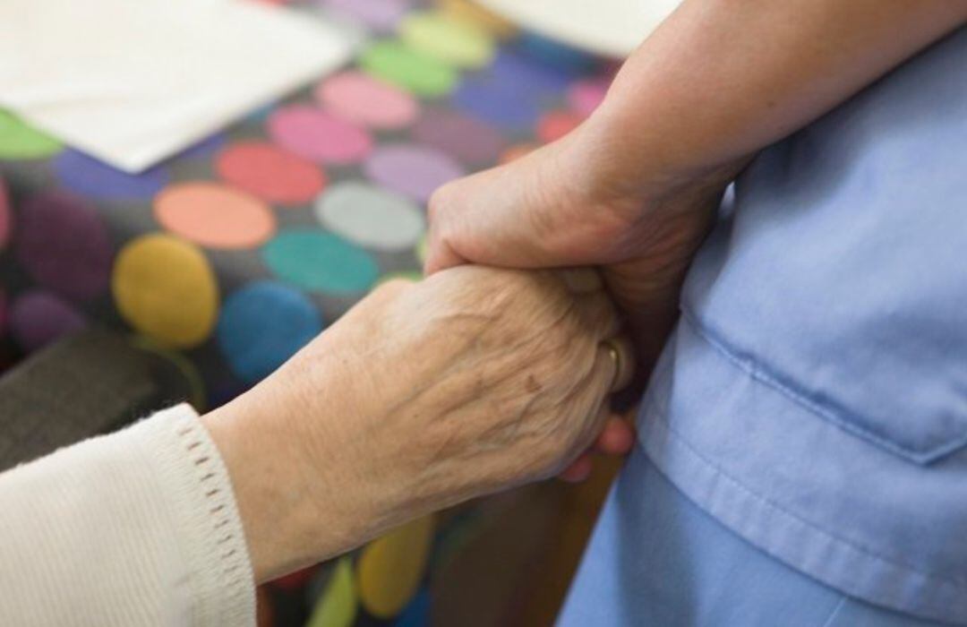 Una trabajadora da la mano a una mujer en una residencia de mayores.