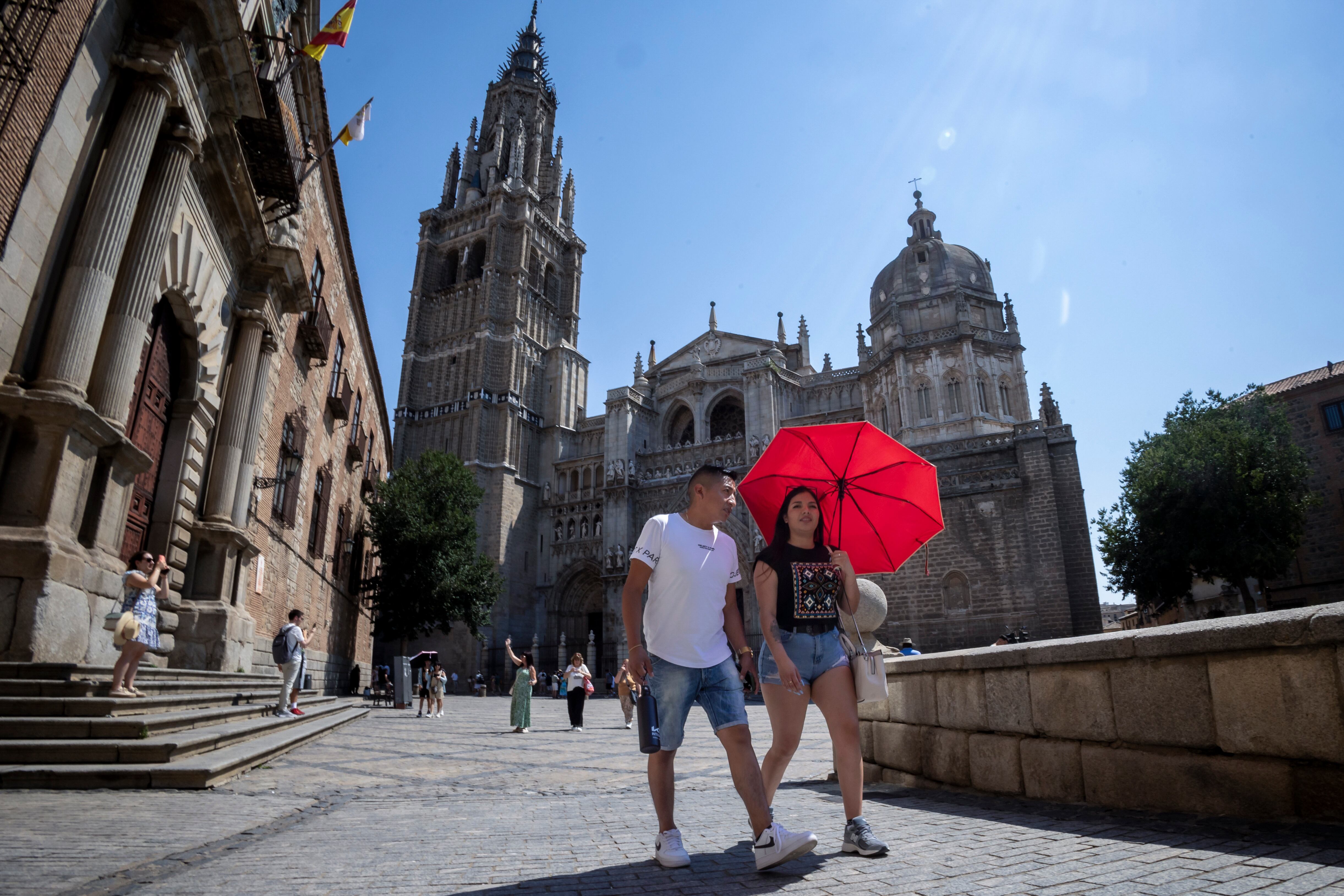 Una pareja se protege del sol mientras pasea por el centro de Toledo.