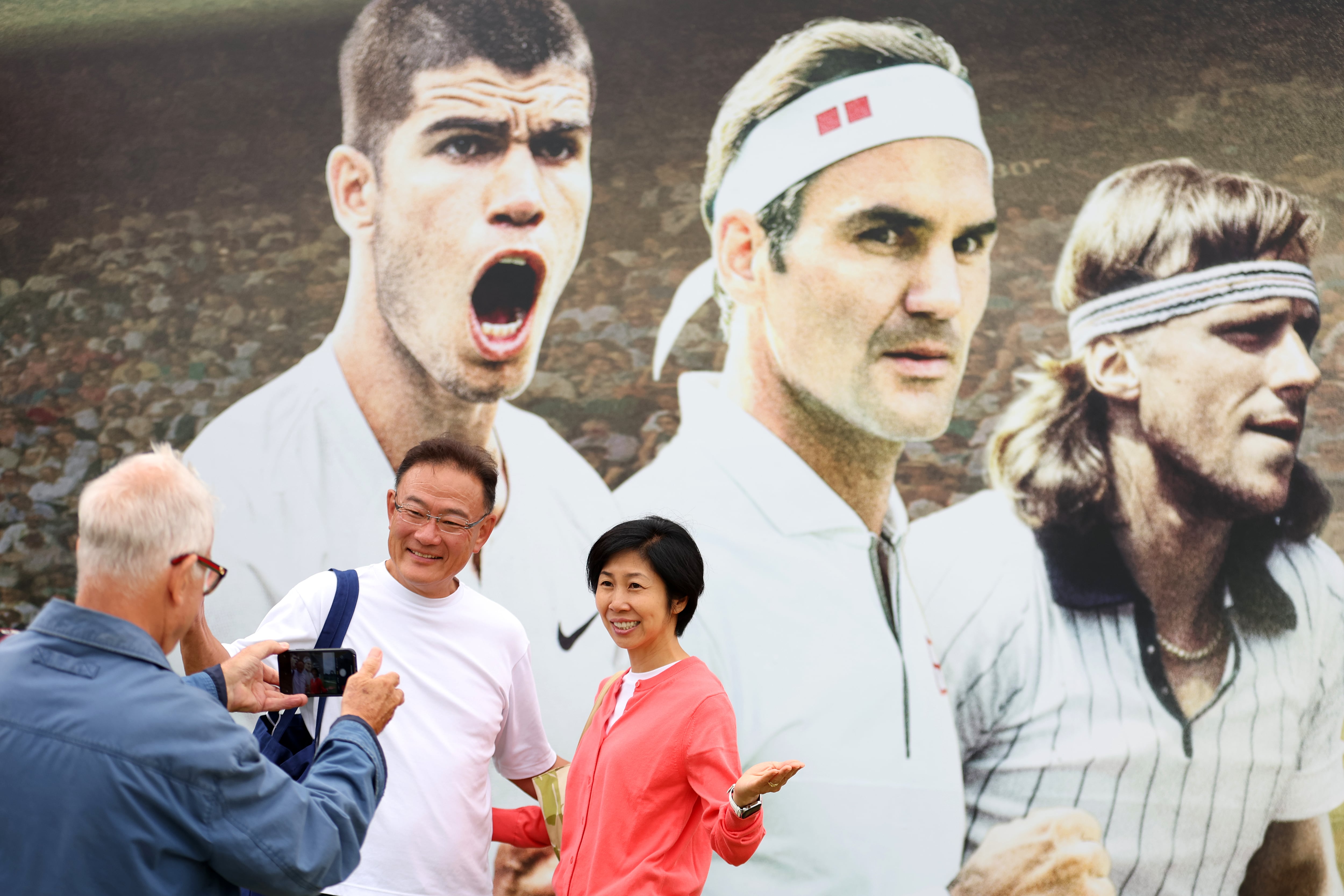 Dos turistas posan con una imagen de Carlos Alcaraz, Roger Federer y Björn Borg