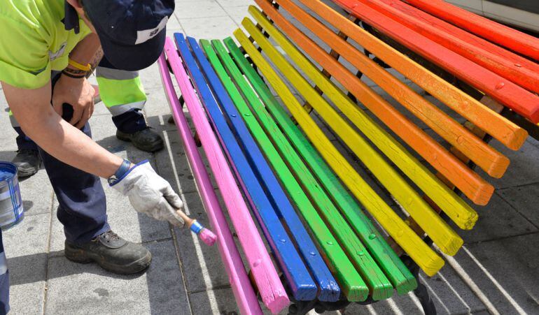 Un operario pinta un banco público con los colores de la bandera de la diversidad sexual