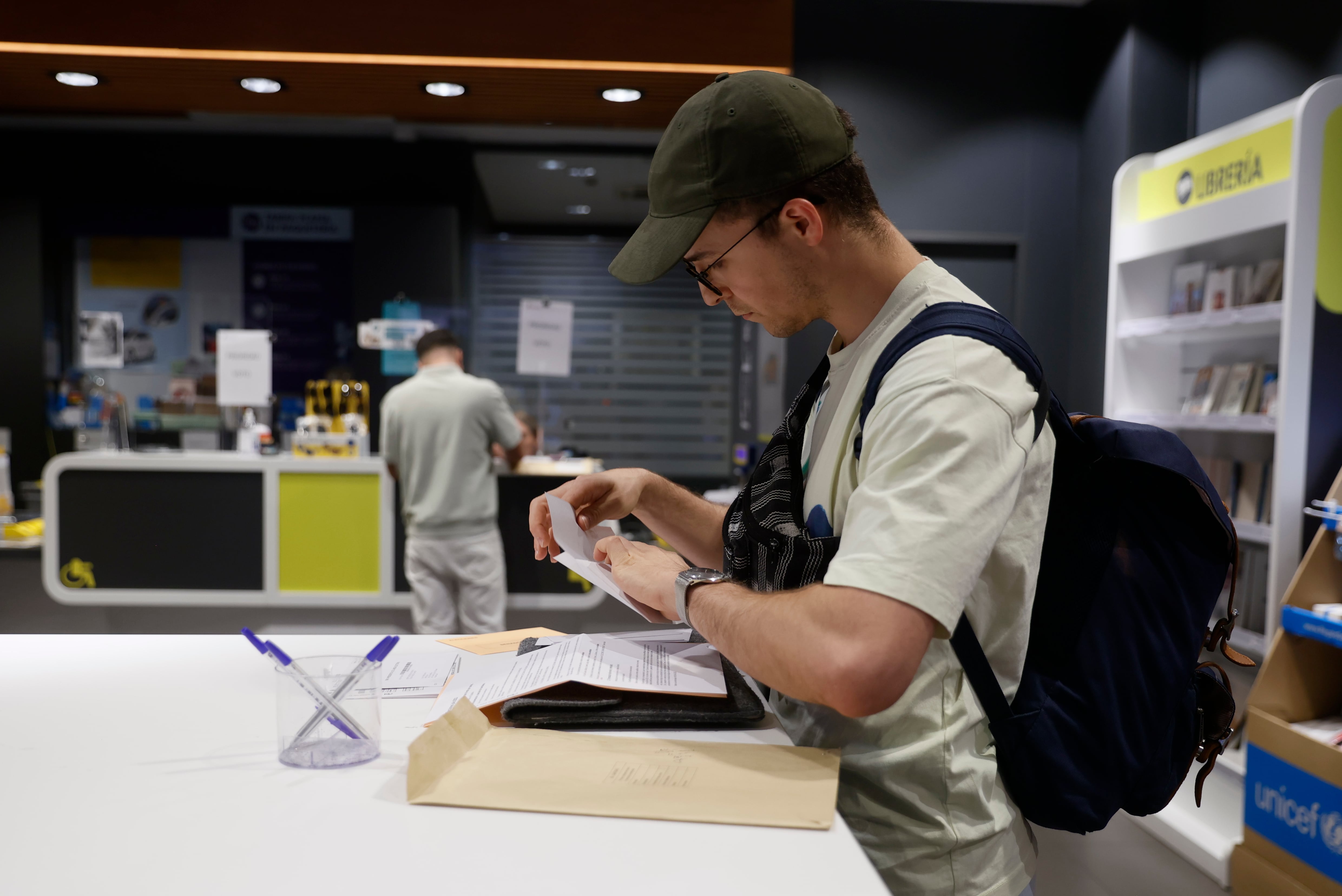 Un hombre cumplimenta la documentación para ejercer el voto por correo en una oficina de Madrid. Oficinas de Correos de grandes ciudades y zonas turísticas abren este fin de semana de forma extraordinaria para facilitar el voto por correo.