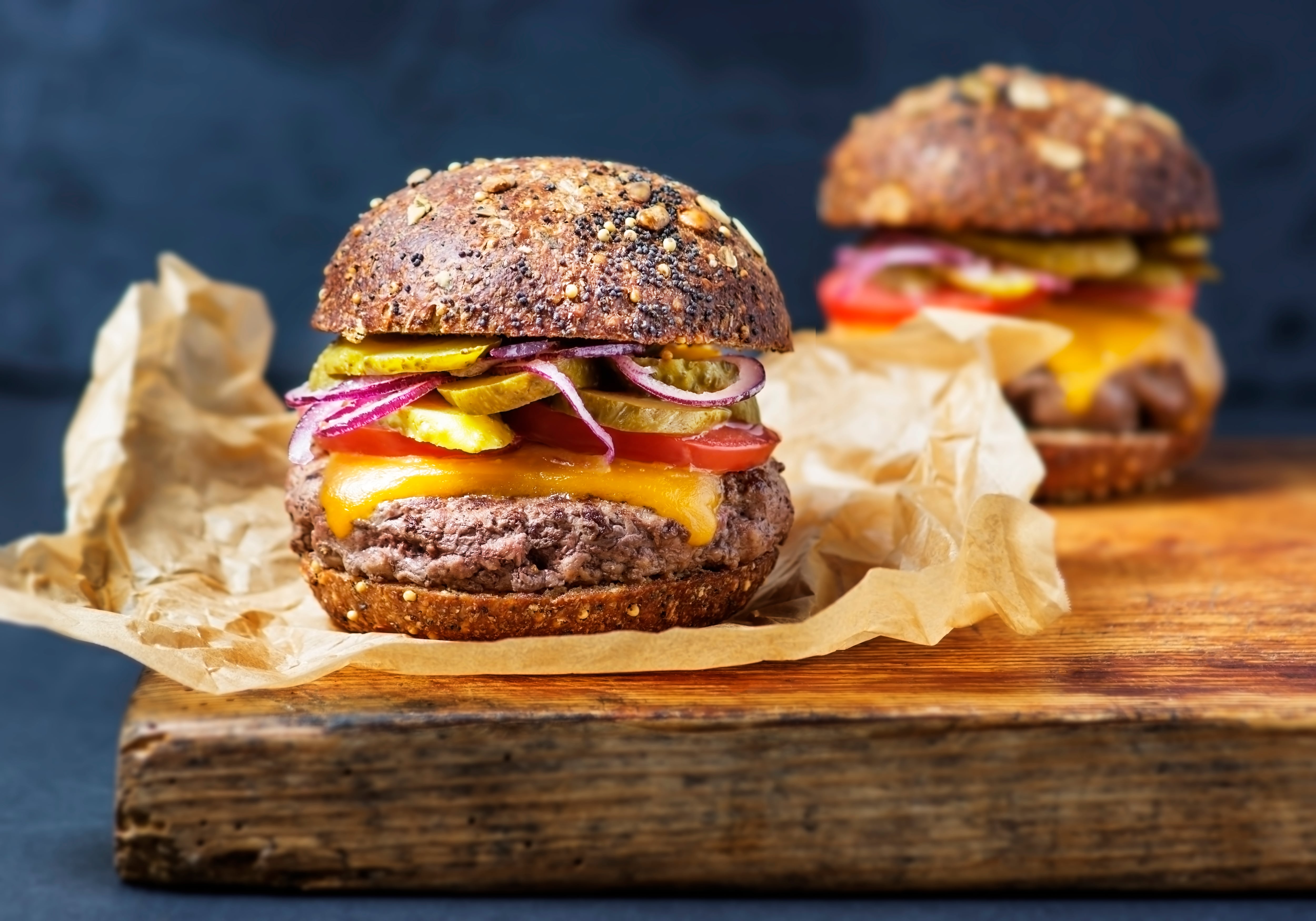 Two burgers on cutting board on black background