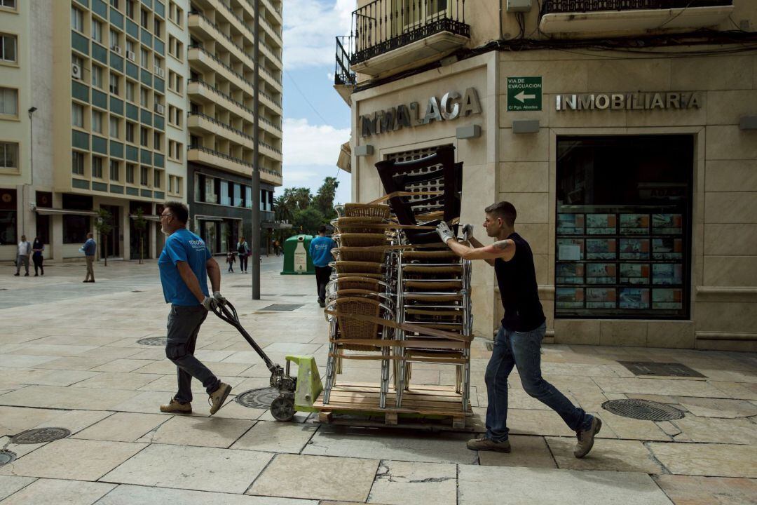 Unas personas transportan las sillas de un establecimiento en Málaga debido a no poder abrir en la fase 0 en la que se encuentra aún esta provincia andaluza, una de las dos que no ha pasado a la fase siguiente de la desescalada en el Estado de Alarma decretado por el Gobierno debido a la crisis de la