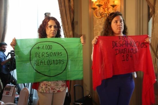 Les dues activistes de la PAH, pujades a la cadira, amb les pancartes a la mà mentre Miguel Arias Cañete parla