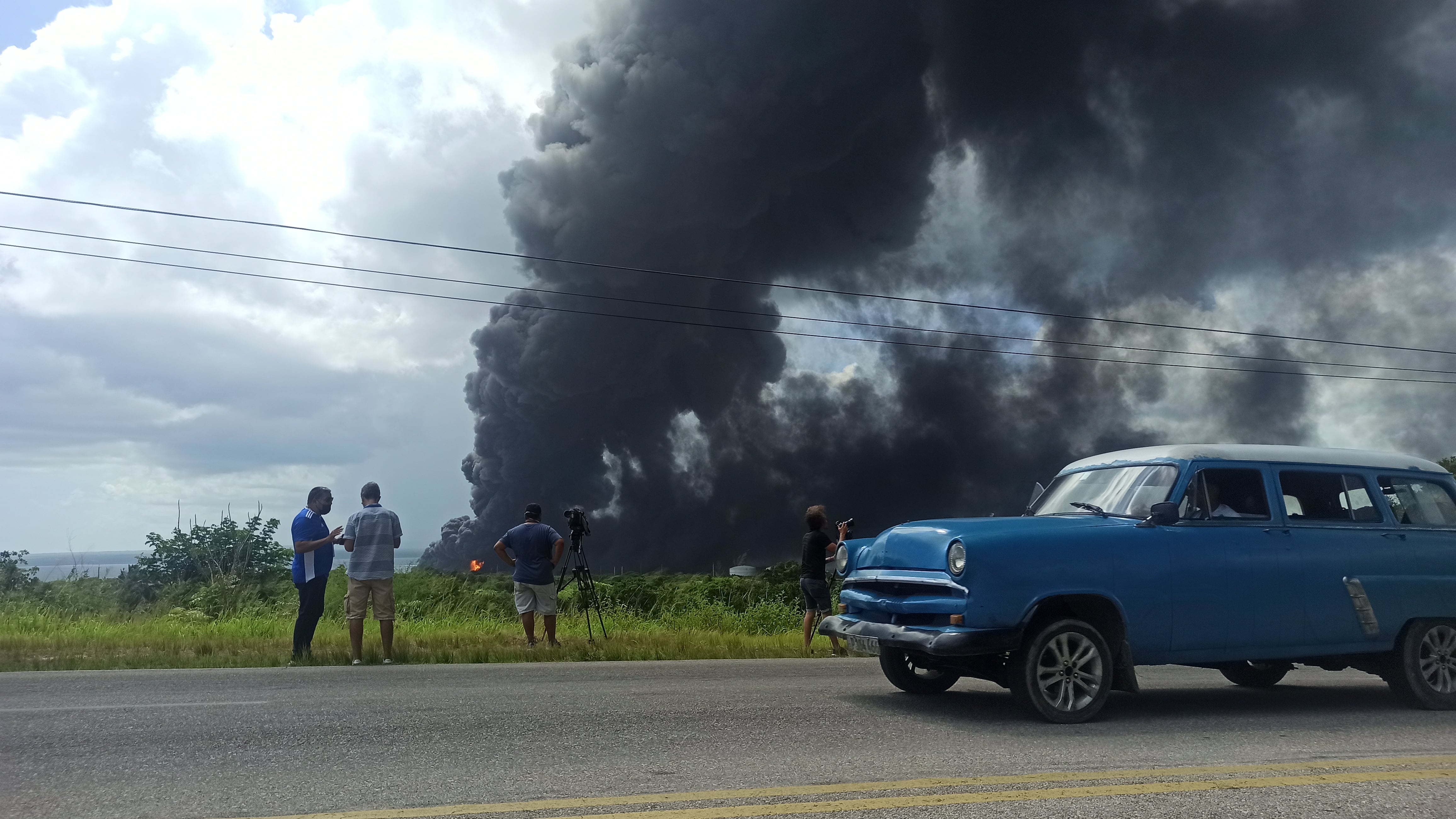 Fotografía de un vehículo mientras cruza frente a la columna de humo generada por el incendio en un depósito de combustible hoy, en Matanzas (Cuba).