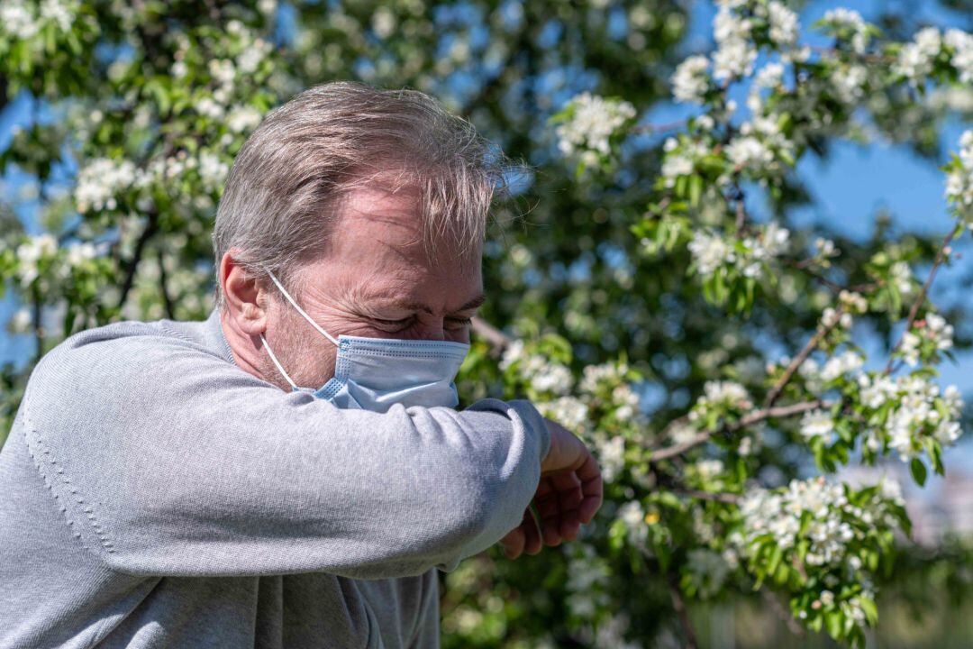 Archivo - Un hombre con mascarilla estornuda debido a la alergia