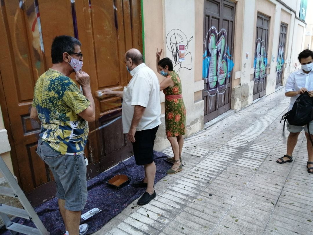 Miembros de la plataforma ciudadana borran los grafitis de una de las puertas del antiguo Cine Ideal