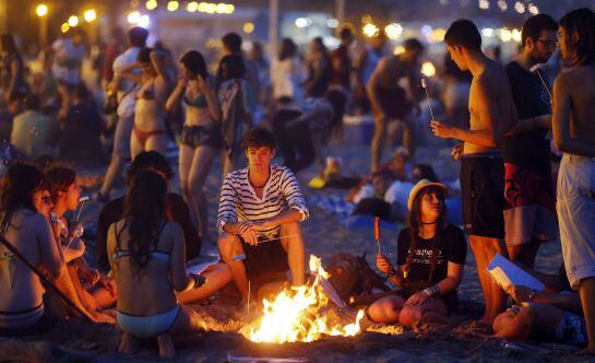 Varios jovenes aguardan alrededor de una hoguera en la playa de la Malvarrosa, en Valencia.