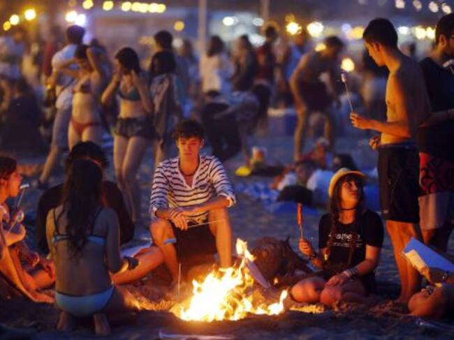 Varios jovenes aguardan alrededor de una hoguera en la playa de la Malvarrosa, en Valencia.