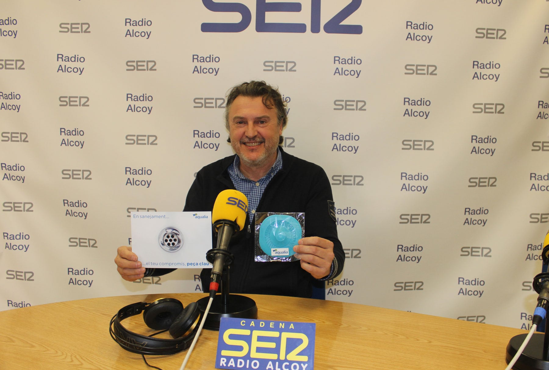 Santi Catalá, en el estudio central de Radio Alcoy, sostiene los elementos de la campaña que ha puesto en marcha Aqualia