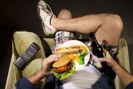 Una persona come una hamburguesa mientras ve la televisión