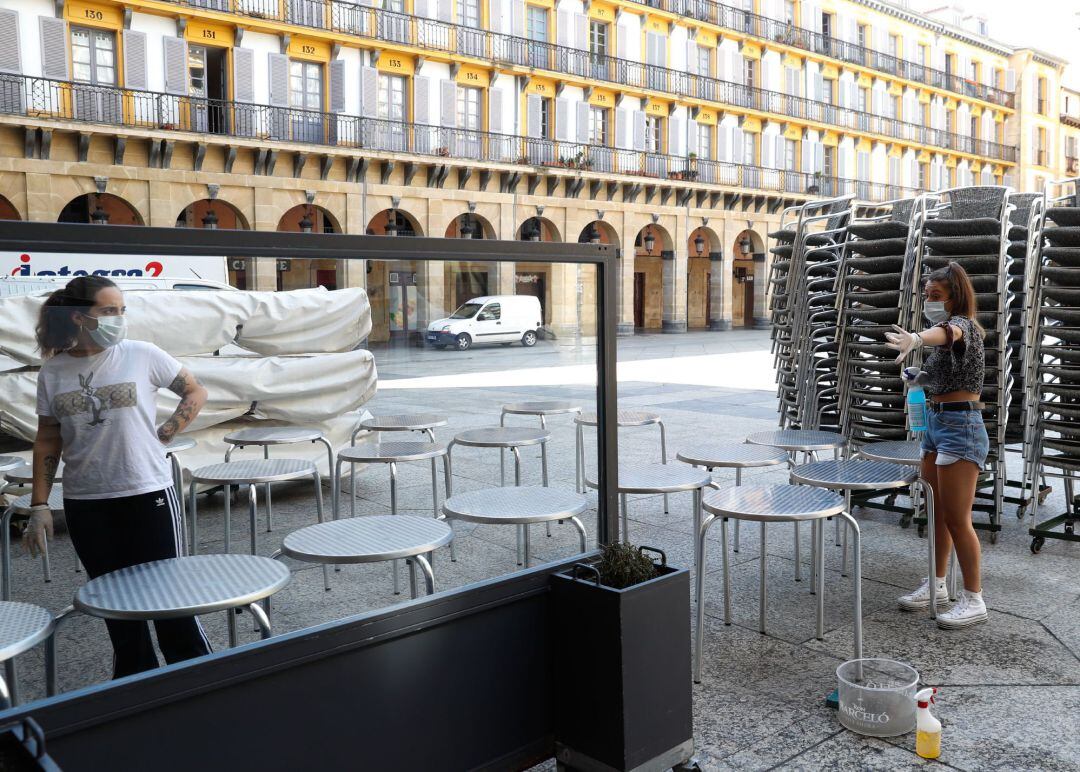 Trabajadoras de un bar de la Parte Vieja de San Sebastián desinfectan el mobiliario de terraza para poder iniciar el servicio.