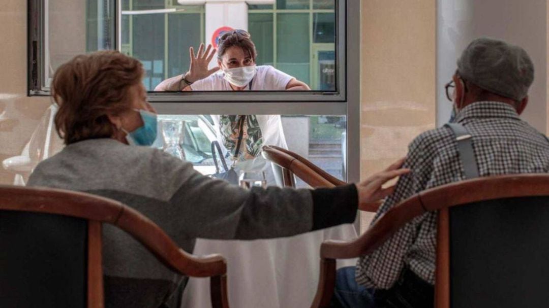 Un familiar saluda desde el exterior a dos mayores en una residencia