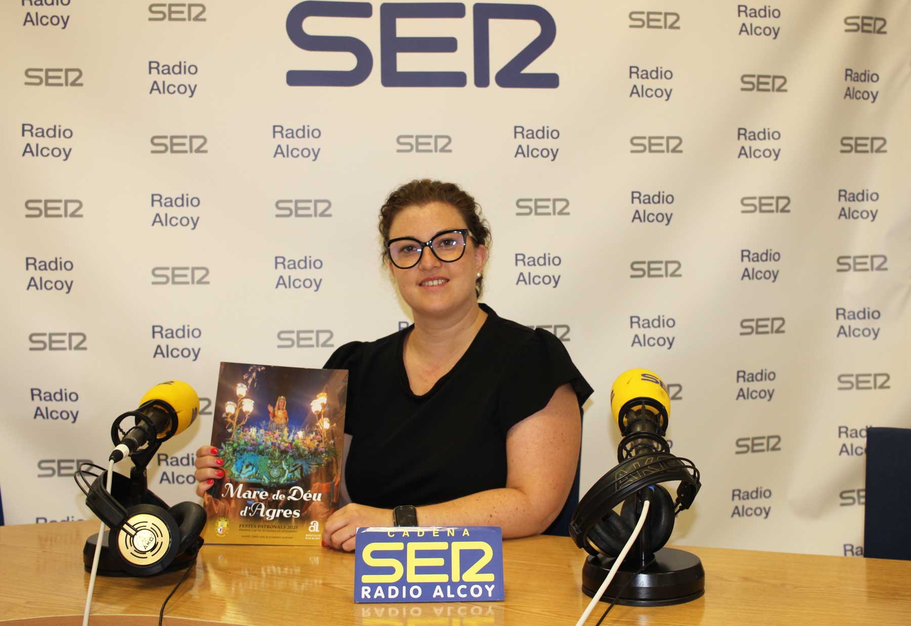 María García Pascual, alcaldesa de Agres, en el estudio central de Radio Alcoy, con un ejemplar de la revista de fiestas