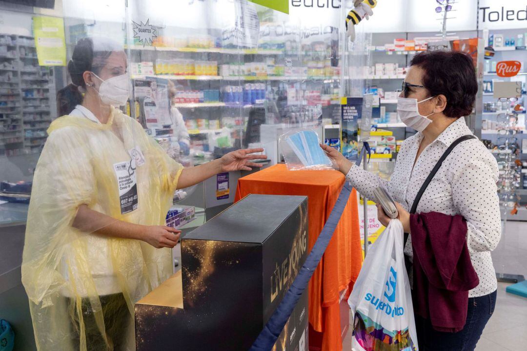 Una empleada de farmacia entrega de forma gratuita dos mascarillas a una pensionista mediante la receta electrónica en una farmacia de Murcia