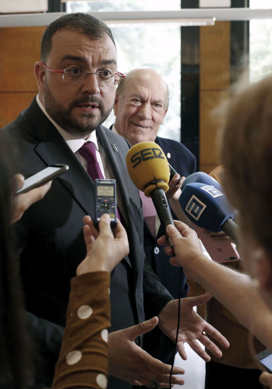 El presidente, Adrián Barbón, atiende a los medios tras sus reuniones con ACOM y el empresario Antonio Suárez, al fondo de la imagen