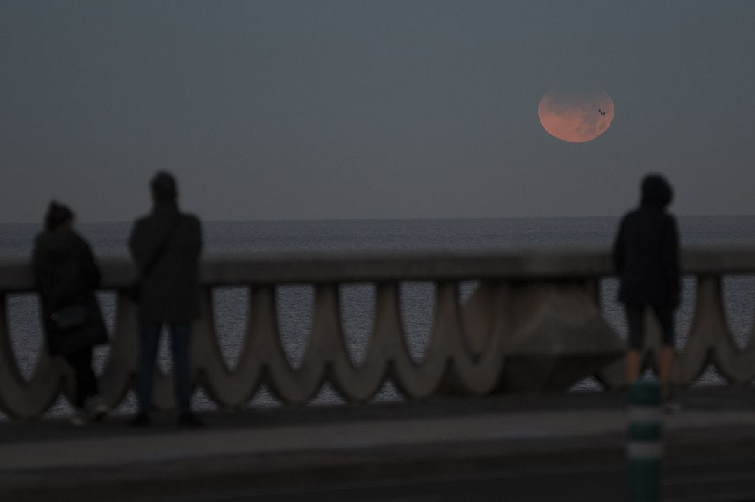 Tres personas observan el eclipse lunar parcial desde A Coruña este 19 de noviembre de 2021.