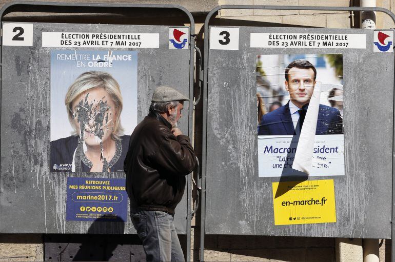 Un ciudadano camina ante los carteles de campaña de Marine Le Pen y  Emmanuel Macron en París