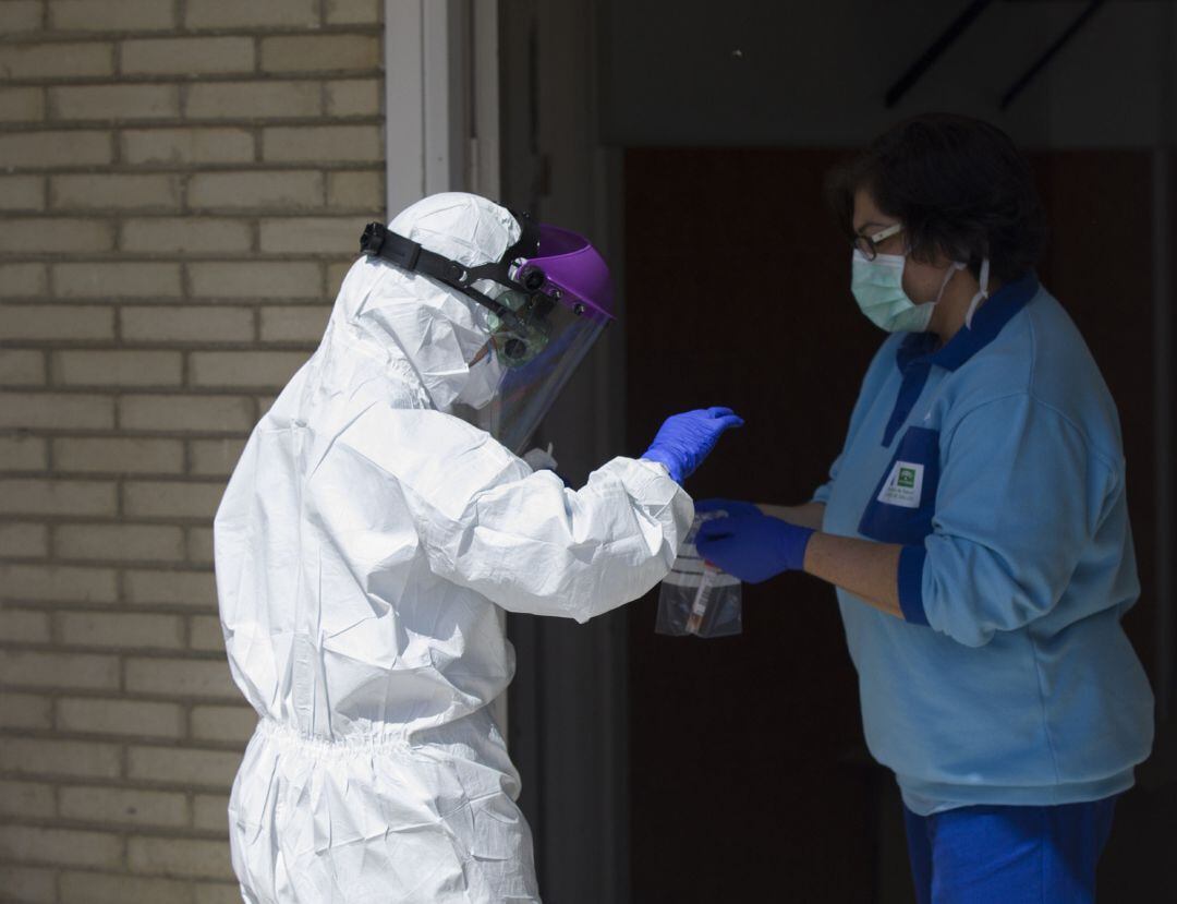 Un sanitario entrega las pruebas a otro, tras realizar una recogida de muestra desde el coche para detectar casos de coronavirus, (Covid-19), en el Hospital Militar de Sevilla