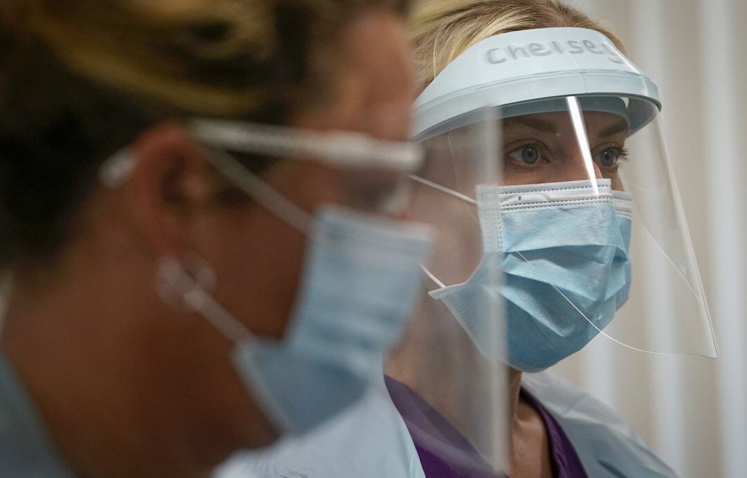 Dos profesionales sanirarias protegidas por una pantalla y mascarilla.