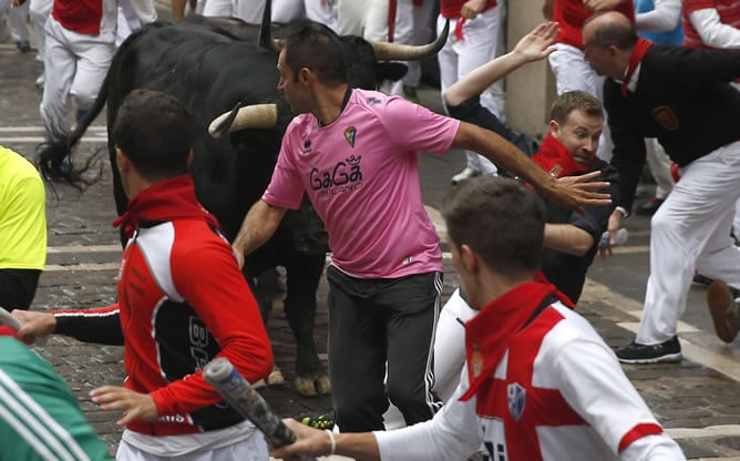 Varios mozos corren delante de los toros de la ganadería de Victoriano del Río Cortés en la calle Mercaderes con la calle Estafeta, durante el tercer encierro de los sanfermines 2014.